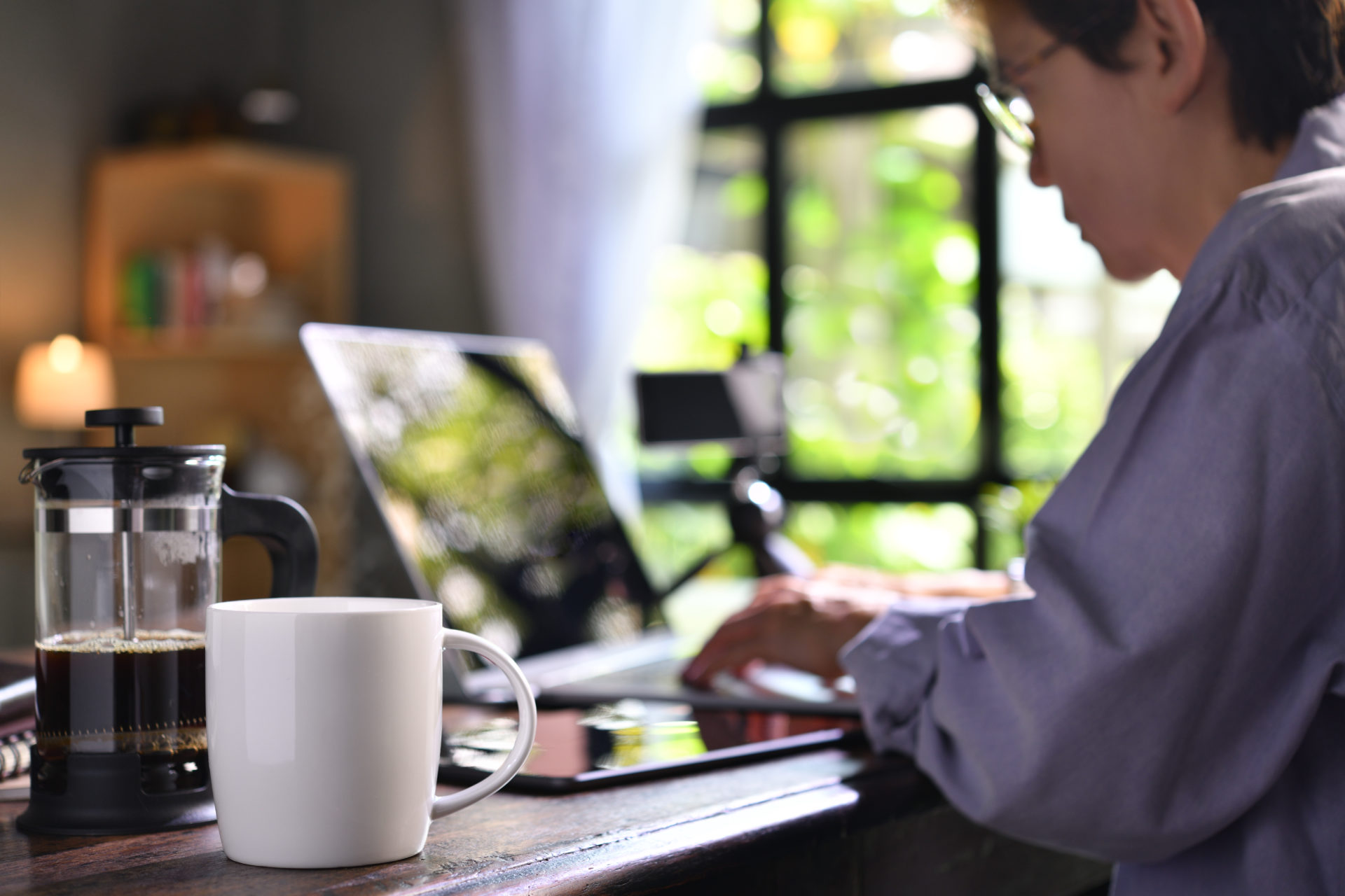 A coffee press and a cup on a work desk with a person working from home