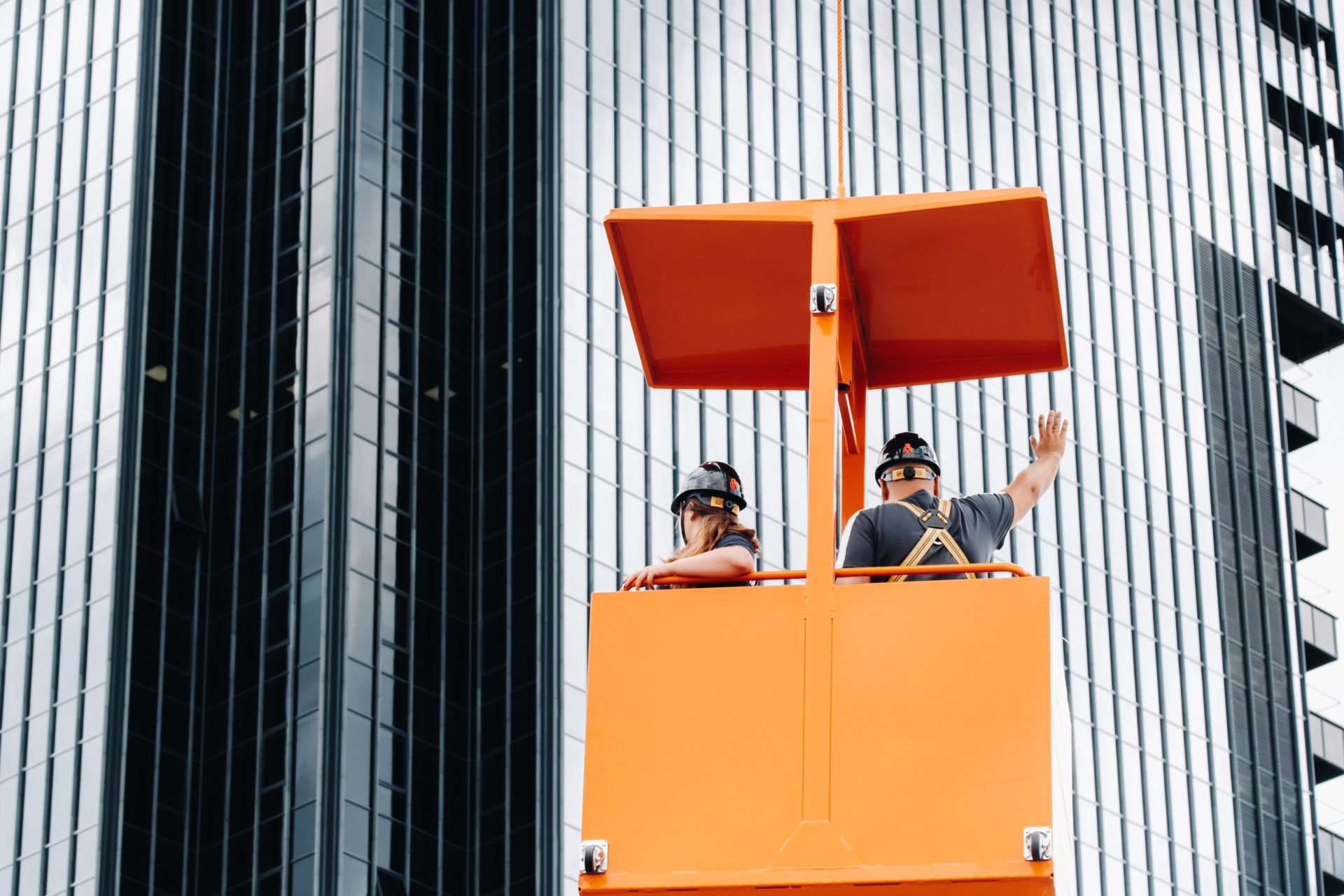 Workers in a construction cradle climb on a crane to a large glass building.The crane lifts the workers in the car seat.Construction Fall Protection